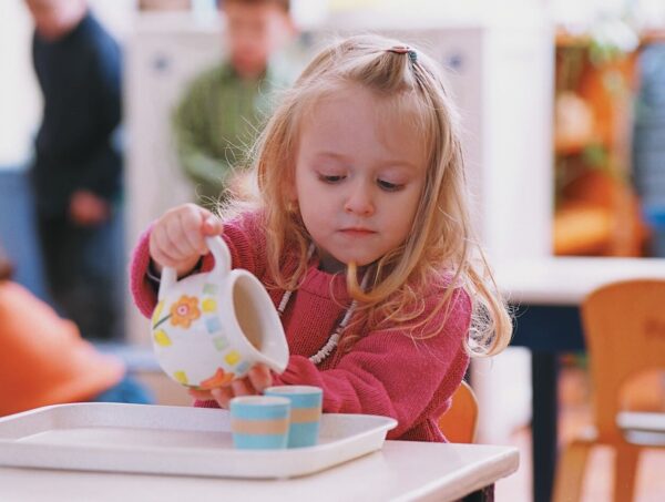 A girl carefully pouring water from a pitcher into a glass, demonstrating concentration and fine motor skills in a Montessori environment.